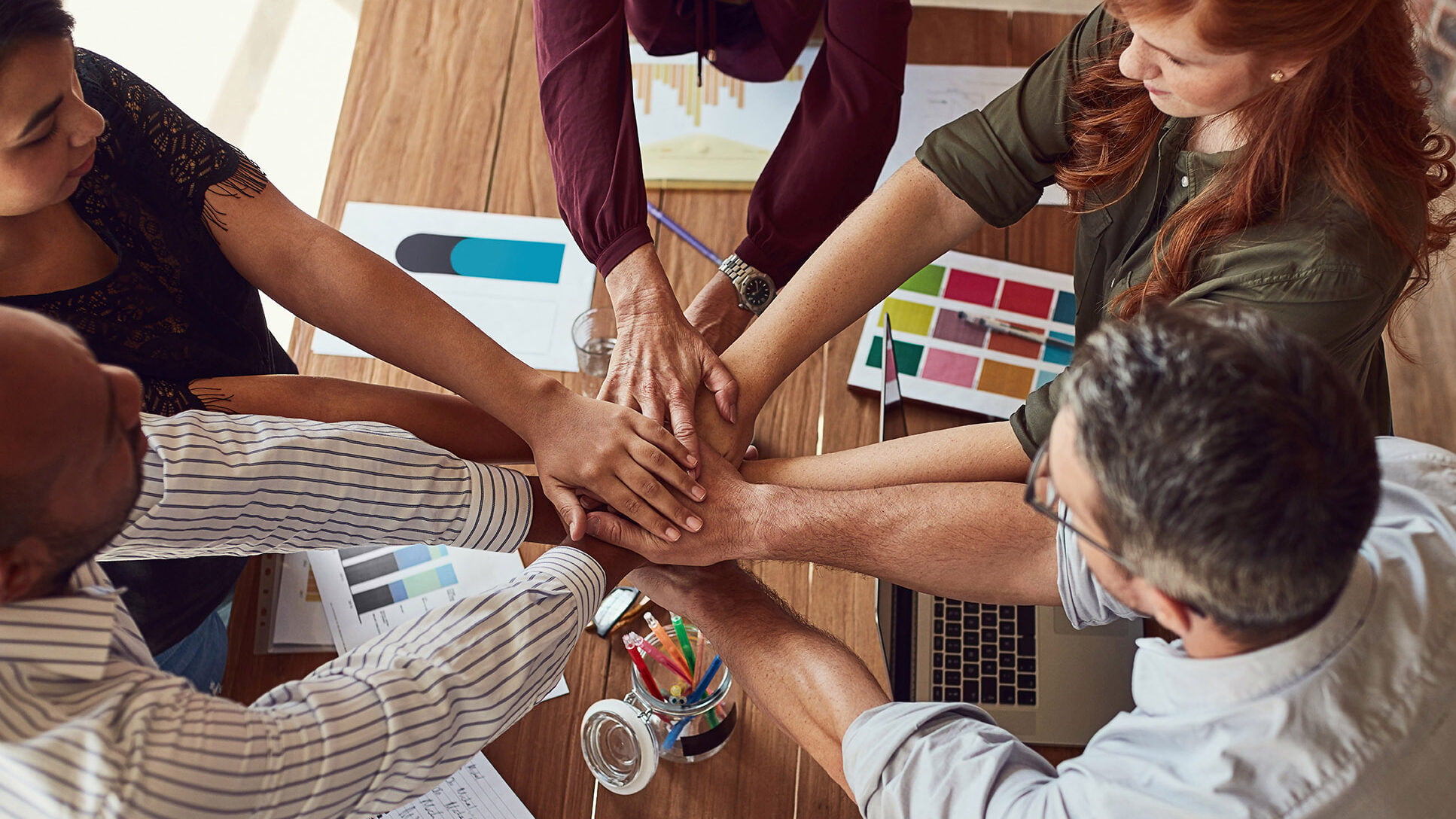 People with hands in center over desk