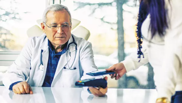 A healthcare worker sits and holds a payment processing terminal in front of a customer.